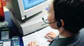 an employee sitting at a desk facing the computer talking on a headset and typing on the keyboard